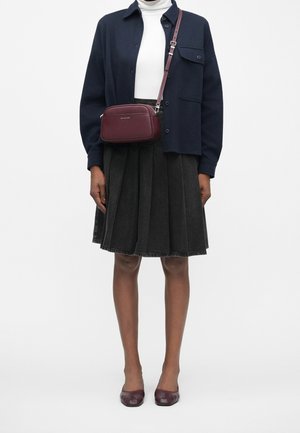 Osoba ubrana w granatową koszulę zapinaną na guziki, białe golf, ciemną plisowaną spódnicę, bordową torebkę na ramię i pasujące bordowe buty.