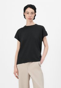 Svart kortärmad T-shirt med rund hals, avslappnad passform och upprullade ärmar, ihopparad med ljusbeigefärgade vida byxor. Enkelt och minimalistiskt design.