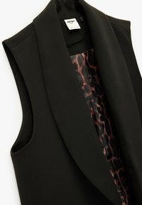 Blazer nero senza maniche con una texture liscia e una fodera in satin con stampa leopardata. Presenta un colletto a reversed e un design minimalista.