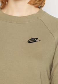 Oliivinvihreä huppari, joka on valmistettu pehmeästä kankaasta ja jossa on musta brodeerattu Nike-logo rinnassa. Klassinen pyöreä pääntie ja raglan-hihat.