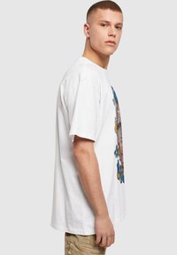 Hvit bomulls t-skjorte med et fargerikt grafisk design av blomster og sommerfugler på fremsiden, med en løs passform og korte ermer.