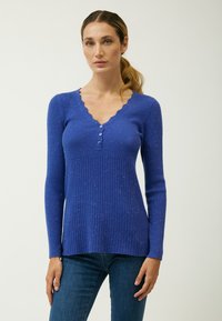 Maglione blu a coste con scollatura a V ondulata, maniche lunghe e quattro bottoni decorativi. Il tessuto presenta una texture screziata per un tocco di originalità.