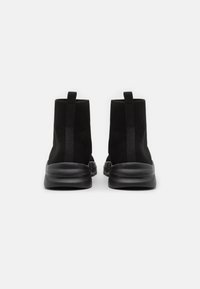 Černé pletené kotníkové boty s těsným střihem, vyznačující se texturovaným svrškem, flexibilní podrážkou a zesílenými poutky pro snadné nazouvání.