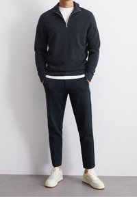 Marinblå stickad tröja med halv dragkedja, kombinerad med mörka byxor och vita sneakers. Texturerad tyg med en figurnära silhuett.