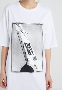 Biała, oversize'owa koszulka z krótkim rękawem z graficznym printem w czarnym i srebrnym wzorze, z napisem "DK NY 1993" oraz gwiazdami.
