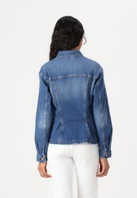 Blue denim jacket with a fitted silhouette, pointed collar, and buttoned cuffs. Features stitching details and a slightly faded finish.