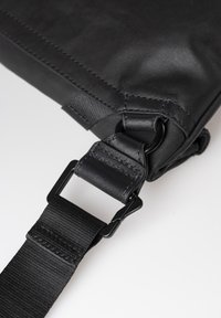 Black bag featuring a textured exterior, adjustable strap with a secure metal buckle, and stitched accents. Compact and practical design details.