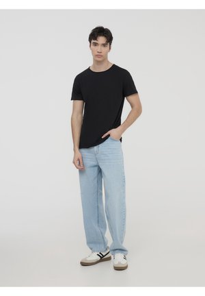 T-shirt nera a maniche corte con scollatura rotonda, abbinata a jeans dritti azzurri e sneakers bianche con accenti scuri.