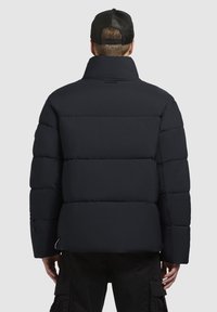 Tumesinine puhvjakiri kõrge kaelusega, väikeste tõmblukudega disain ja elastsed mansetid. Vasakul varrukal on tõmblukuga tasku.