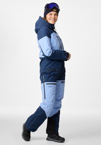 Skianzug in Dunkel- und Hellblau, mit durchgehendem Reißverschluss, mehreren Taschen und einer Kapuze. Strukturierter Stoff mit kontrastierenden Farbpaneelen.