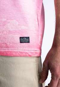 Camiseta de algodón rosa con un patrón sutil, que presenta una etiqueta negra en el dobladillo. El diseño es casual y se ajusta estrechamente al cuerpo.