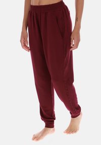 Pantaloni jogger bordeaux con fascia elastica in vita, tasche laterali e cuciture decorative sui lati. Realizzati in tessuto morbido con vestibilità comoda.