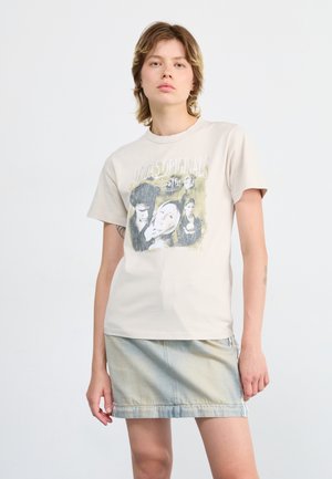 Beige T-shirt met korte mouwen met een grafische print van gezichten en tekst, gecombineerd met een lichte denim rok met een franjezoom.
