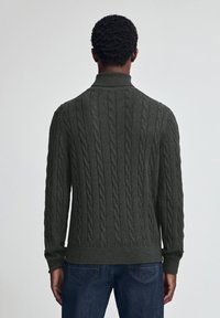 Dunkelgrüner Grobstrickpullover mit hohem Kragen und gerippten Bündchen, ausgestattet mit einem strukturierten Muster und einer figurnahen Passform.