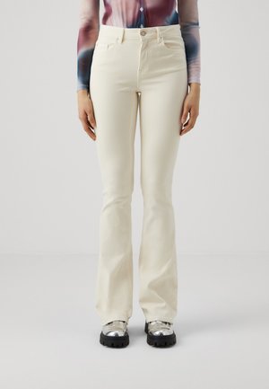 White flared jeans with a smooth texture, five-pocket design, and a front button closure, paired with shiny silver platform shoes.