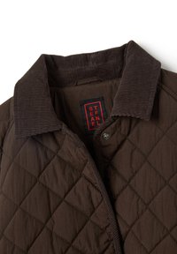 Braune gesteppte Jacke mit einem Cordkragen, die rautenförmige Muster, Metallknöpfe und ein rotes Etikett mit dem Text "STEFANEL" aufweist.