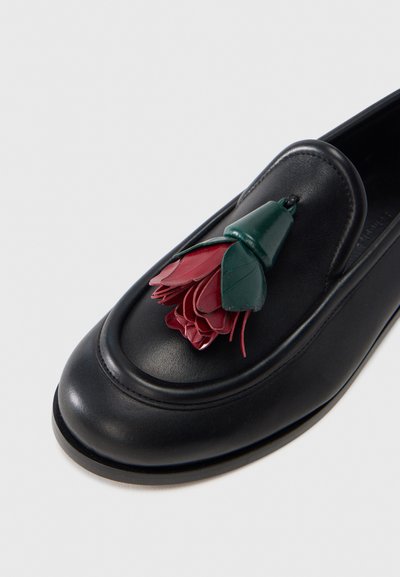 Mocassim em couro preto com um ornamento floral em vermelho e verde, acabamento liso e design de biqueira arredondada.