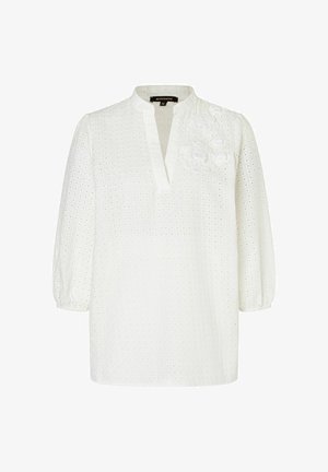 White blouse featuring a V-neckline, puffed sleeves, and embroidered floral detail. Made of textured fabric with eyelet pattern.