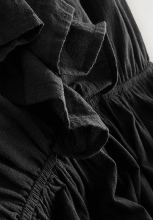 Schwarzes Kleid aus Stoff mit Rüschendetails, weicher Textur, gerafftem Taillenbereich und subtilen Variationen in der Stoffdicke.