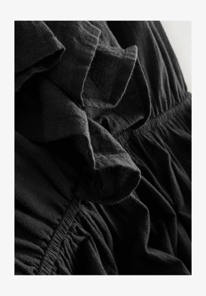 Robe en tissu noir avec des détails froncés, texture douce, taille froncée et variations subtiles d'épaisseur du tissu.