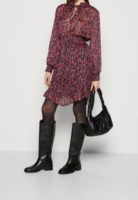 Abito floreale con una base nera, accenti rosa, maniche lunghe e orlo arricciato. Abbinato a stivali alti fino al ginocchio in pelle nera e una borsa nera.