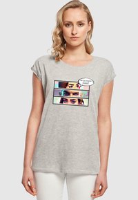 Lys grå bomulds t-shirt med rulleærmer, der har et tegneserie-lignende grafisk motiv af tre øjne og en tale-boble med tekst.