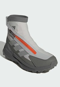 Grå sportkänga med högt skaft, orange dragkedja som detalj och robust sula. Ovansidan har en strukturerad yta och andningsbart material.