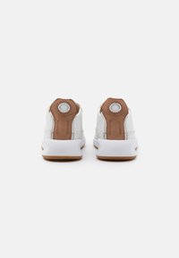 Zapatillas blancas con acentos marrones, que presentan un tirador en el talón de cuero texturizado, ojales redondos y una suela de goma. Diseño minimalista y acabado semimate.