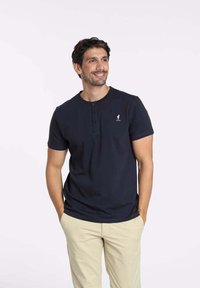 T-shirt henley marine en coton, avec un col rond, une patte de boutonnage à trois boutons et un petit logo sur la poitrine gauche. Coupe décontractée.
