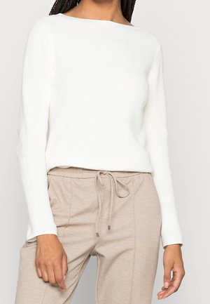 Pull blanc côtelé à manches longues avec un col bateau, associé à un pantalon beige à cordon de serrage, présentant une texture lisse et une coupe décontractée.
