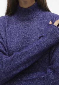 Maglione a collo alto viola realizzato in tessuto a maglia testurizzata, con maniche lunghe dotate di fori per le dita per una maggiore copertura.