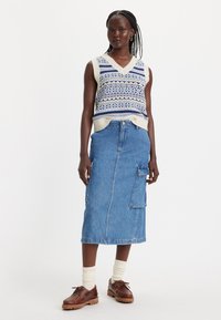 V-hals strikket vest med blå og cremefarvet mønstrede detaljer, parret med en denim midi nederdel med en sidelomme og brune snørebåndssko.