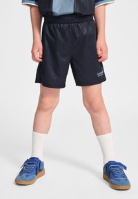 Marina atletiska shorts med vertikala ränder, elastisk midja och logodetalj. Matchas med blå sneakers och vita ribbade strumpor.