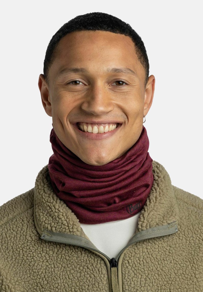 Burgundy neck gaiter made of stretchy fabric, layered and textured, worn over a beige fleece jacket with a zip. Features a logo detail.