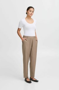 Haut blanc à manches courtes associé à un pantalon marron ajusté. Le pantalon est doté de poches latérales et d'une texture lisse. Des chaussures plates noires complètent l'ensemble.