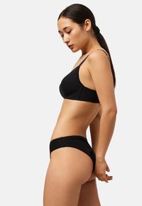 Conjunto de sujetador negro y ropa interior a juego. El sujetador tiene tirantes finos y un diseño sin costuras; la ropa interior presenta un borde festoneado y un corte clásico tipo bikini.