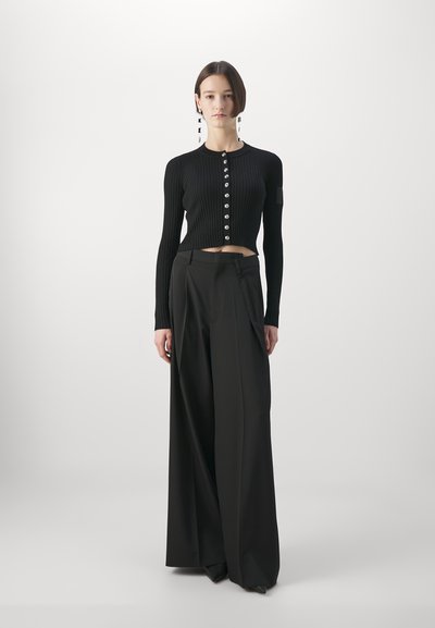 Zwarte geribde cardigan met knoopsluiting en cropped ontwerp, gecombineerd met zwarte wide-leg broek met plooien en zijzakken.