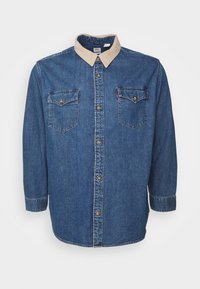 Jeansskjorta i blått med en krage i tan kordflård, två bröstfickor med knappstängning, och långärmar som är uppvikt till 3/4 längd.