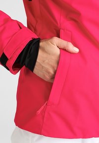 Giacca impermeabile rosa con tasca con zip, polsini regolabili e fodera interna nera a contrasto. Tessuto liscio, taglio moderno.