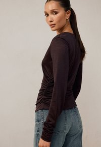 Duga majica s tamnosmeđim rukavima s detaljima naboranja sa strane, od mekane tkanine, okruglog izreza, uparena sa svijetloplavim trapericama visokog struka.