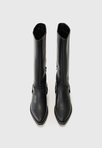 Botas de cuero negro hasta la rodilla con punta afilada, textura lisa y una correa decorativa con detalles metálicos cerca de la base.