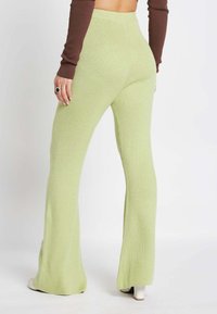 Lichtgroene geribbelde gebreide flared broek met een hoge taille, voorzien van een soepele textuur en een getailleerd silhouet, gecombineerd met witte hakken.