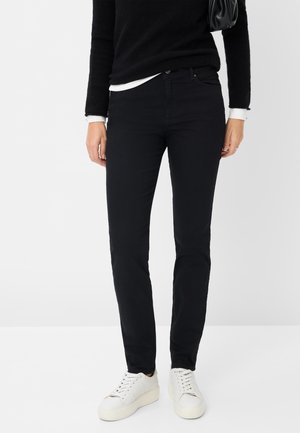 Schwarze, schmal geschnittene Jeans aus weichem, dehnbarem Stoff, mit fünf Taschen und einem klassischen Reißverschluss. Kombiniert mit weißen, strukturierten Sneakers.