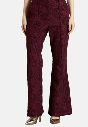 Pantalones acampanados burdeos con un patrón floral texturizado, cintura alta y detalles de pliegue frontal. Combinados con tacones metálicos.