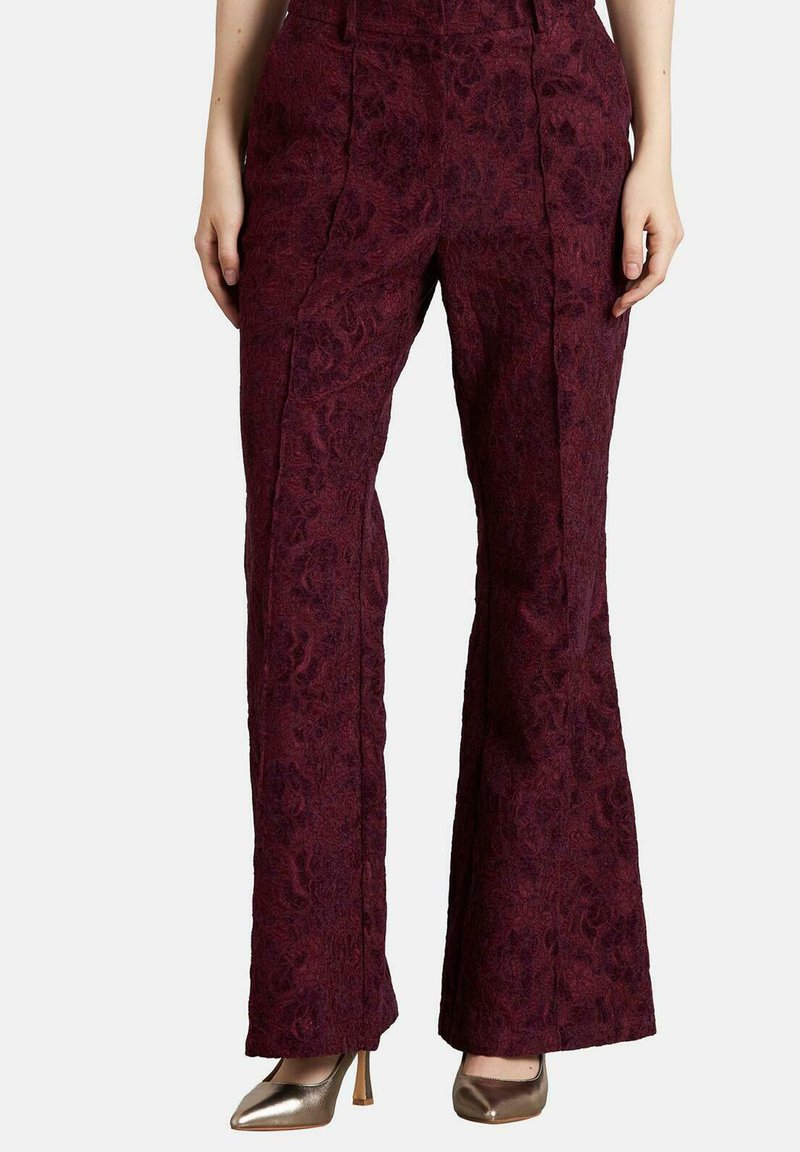 Pantalones acampanados burdeos con un patrón floral texturizado, cintura alta y detalles de pliegue frontal. Combinados con tacones metálicos.
