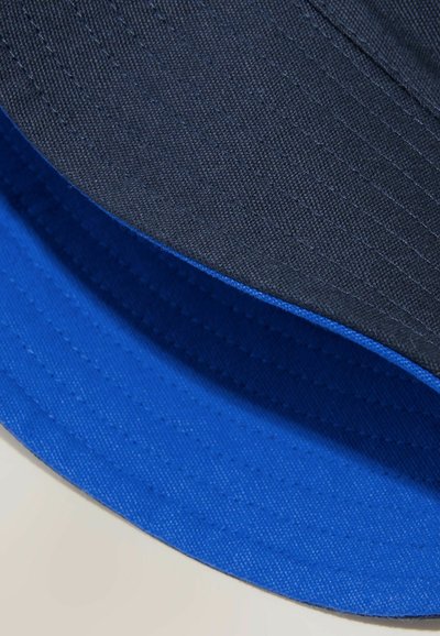 Deux bob se chevauchant avec des bords cousus, l'un noir sur le dessus et l'autre bleu vif en dessous, présentés sur une surface claire.