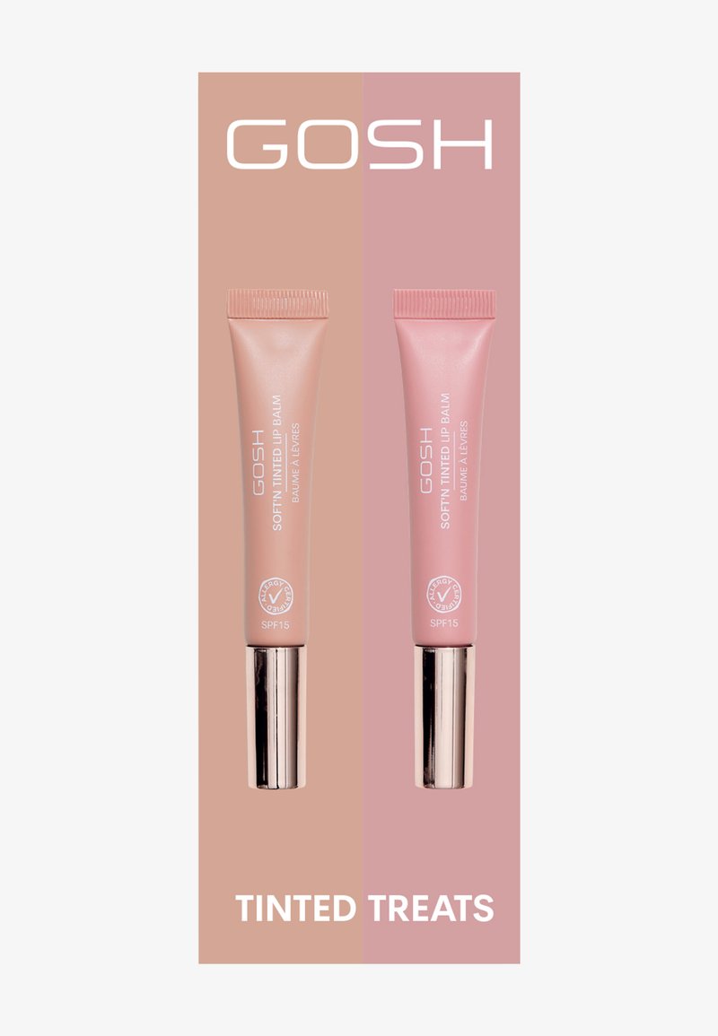 Due tubetti di GOSH Soft’n Tinted Lip Balm, uno rosa pallido e uno rosa tenue, con dettagli argentati, su uno sfondo bicolore. SPF 15 indicato.