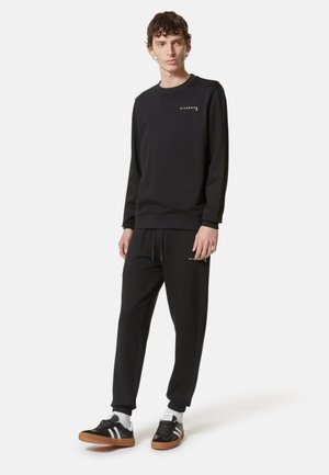 Felpa nera e pantaloni della tuta in misto cotone, con polsini elasticizzati, colletto tondo e dettagli con logo sul petto e sulla gamba.