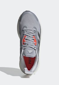 Chaussure de course Adidas grise avec semelle blanche, doublure intérieure rouge et lacets gris vue de dessus.