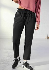 Pantalon de sport noir à coupe ample, avec une ceinture élastique et un cordon de serrage ajustable. Associé à des baskets noir et blanc.